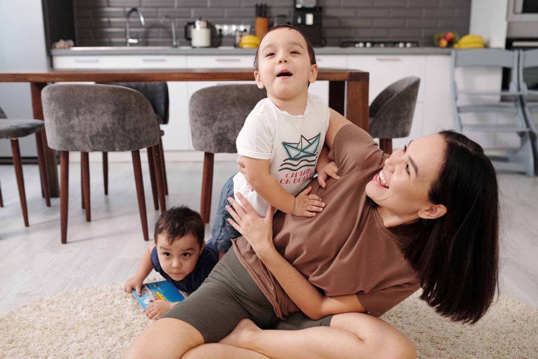 A helper laughing on the floor with two young children at home