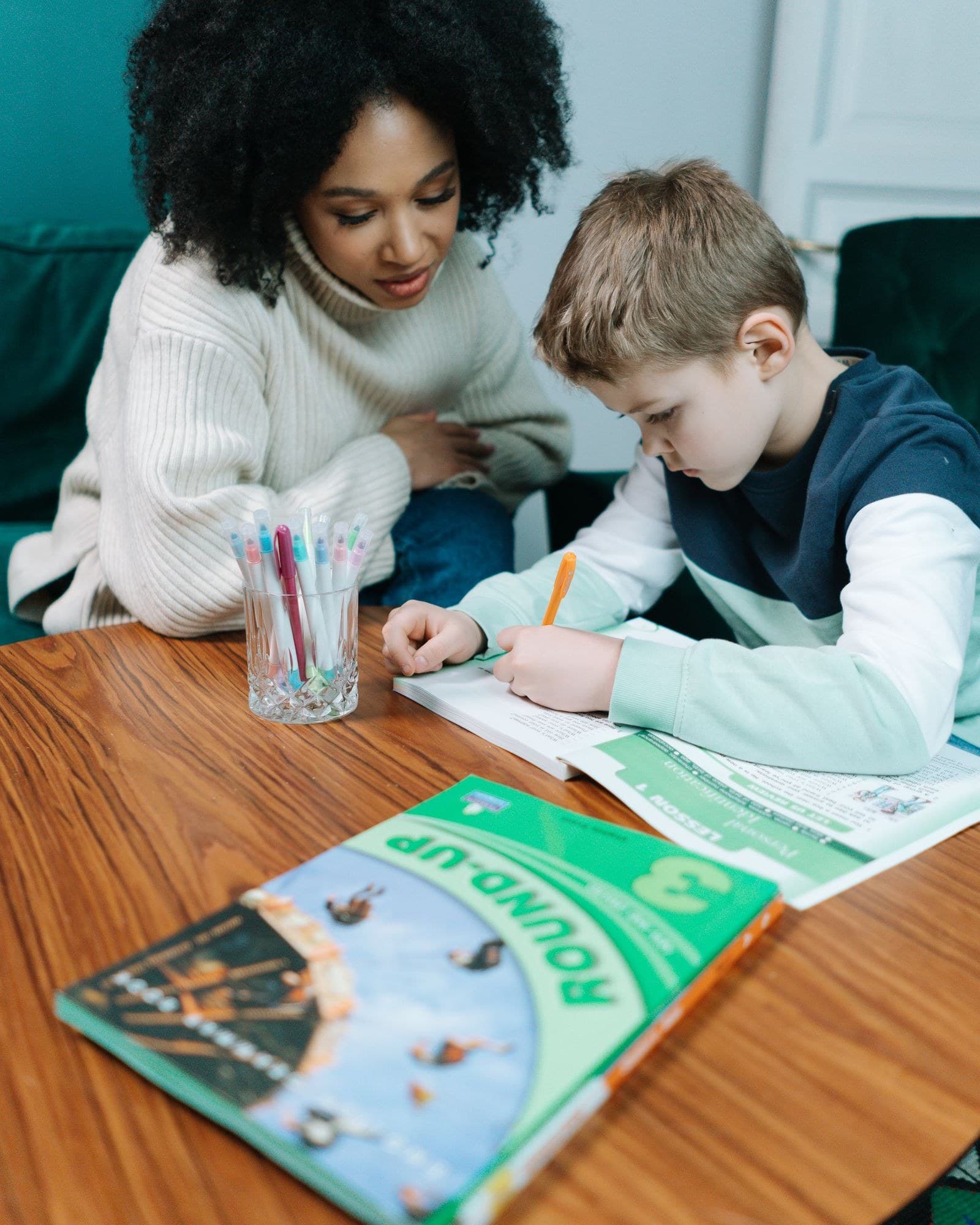 A helper helping a child with homework at the kitchen table